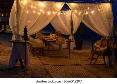 installation with white curtain and light  around a table for a dining experience on the beach at night