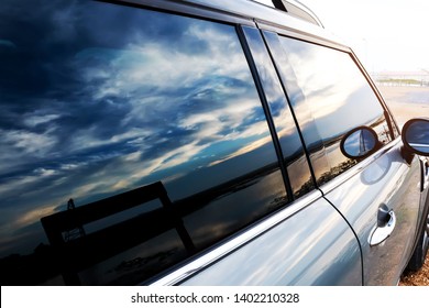 Installation Of Windshield Protective Film. Black Light Film On The Car Glass The Windshield Is Attached To The Side Mirror And Can See The Reflection Of The Sea, The Sunset Sky.