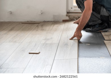 Installer fitting light laminate panels over insulating underlayment during apartment renovation, close-up of hands working on floating floor assembly.