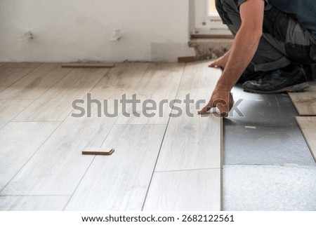 Installer fitting light laminate panels over insulating underlayment during apartment renovation, close-up of hands working on floating floor assembly.