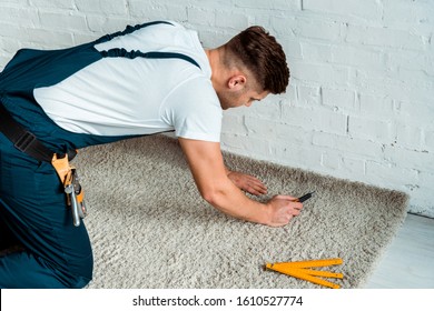 installer in overalls holding cutter near carpet