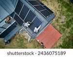 Installers building photovoltaic solar module station on roof of house. Men electricians in helmets installing solar panel system outdoors. Concept of alternative and renewable energy. Aerial view.