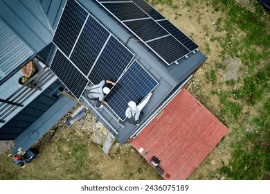 Installers building photovoltaic solar module station on roof of house. Men electricians in helmets installing solar panel system outdoors. Concept of alternative and renewable energy. Aerial view.