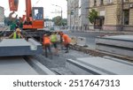 Installing concrete plates by crane at road construction site timelapse. Industrial workers with hardhats and uniform. Reconstruction of tram tracks in the city street