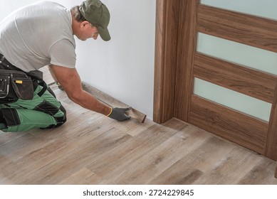 Installing elegant plastic baseboard, showcasing skilled craftsmanship in home improvement and renovation. Detailed view of pro floating floor work, fitting trim for seamless interior finish.