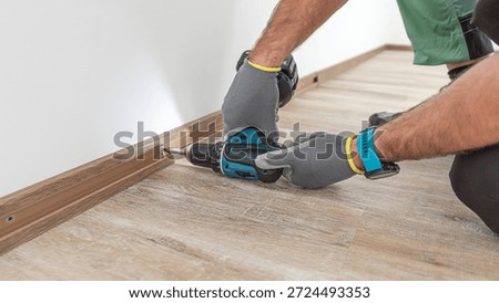 Installing elegant plastic baseboard, showcasing skilled craftsmanship in home improvement and renovation. Worker using a screwdriver to mount skirting board, plinth.
