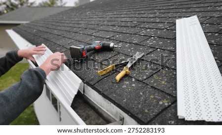 Installing gutter guard on a house roof with tools, home maintenance concept. Home improvement work on a roof installing gutter protection.
