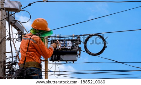 Installing Internet Cable and Telephone Network System, Technician on ladder is Repairing and Maintenance Fiber Optic lines in Splitter Box on Electric Pole against Blue Sky Background
