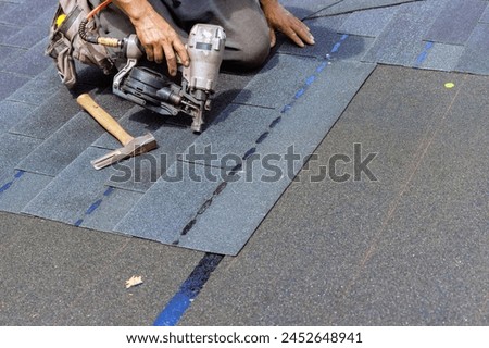 Installing new bitumen shingles using an air nail gun on roof of house