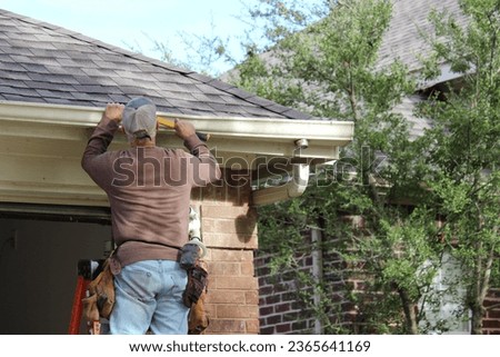 Installing roof gutters; Worker Attaching Aluminum Rain Gutter and Down Spout; Contractor installing gutters on a residential building