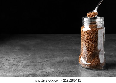Instant Coffee And Spoon Above Glass Jar On Grey Table Against Black Background. Space For Text