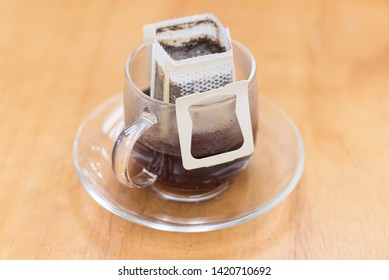 Instant Drip Coffee Using Paper Type Filter With Beans Into A Transparent Glass Cup On Wooden Background.