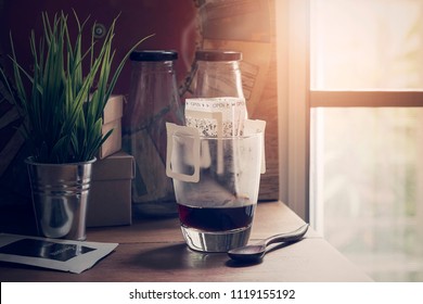Instant freshly brewed cup of coffee or paper dripping bag on a cup on wooden table with sunlight in the morning