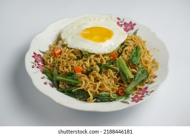 Instant Noodle Dish Topped With Vegetables And Fried Eggs On A Plain White Background