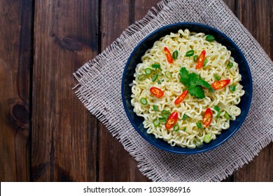 Instant Noodles On Top With Chili ,spring Onion And Cilantro In Dark Blue Bowl  On A Sack In Wooden Background,Top View Photo