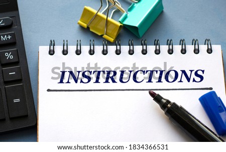 INSTRUCTIONS word is written in a notebook with a marker, calculator, clamps and cactus. Business concept