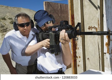Instructor assisting woman aiming with gun at firing range