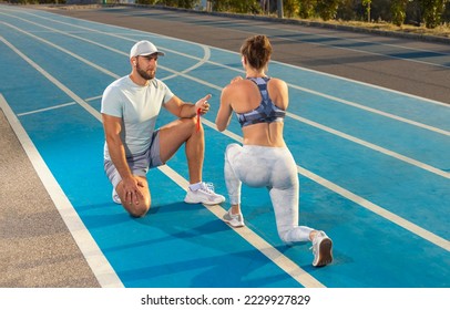 Instructor and athlete runner on the track. The athletics marks the time in the plank exercise on a stopwatch. Fitness trainer and mentee. - Powered by Shutterstock