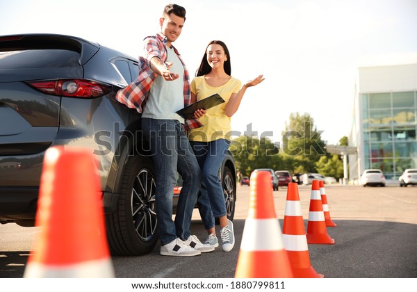 Instructor with clipboard and his student near car\
outdoors. Driving school\
exam