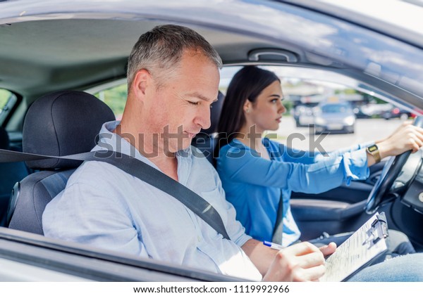 Instructor of driving school giving exam\
while sitting in car. Student driver taking driving test. Driving\
instructor and woman student in examination\
car