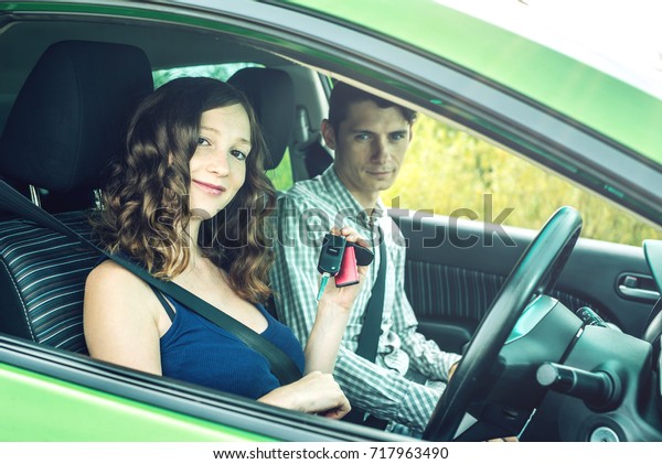 Instructor gives the beginner the car key.\
A woman taking an exam at the driving\
school