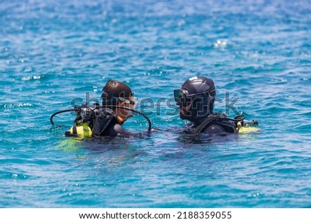 Instructor giving scuba diving lessons to a kid. Scuba diving Instructor teaching a little boy to dive. Diver course. Two scuba divers in shallow Sea. Divers dressed in diving suit, aqualung.