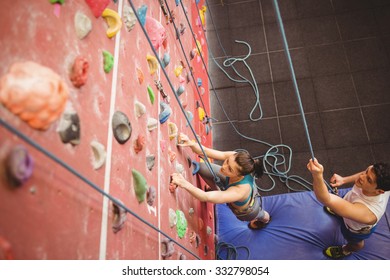 Instructor Guiding Woman On Rock Climbing Wall At The Gym