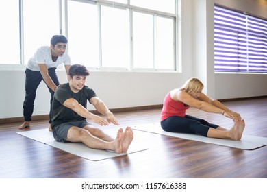 Instructor helping beginners to do forward bend pose at yoga class. Man and woman practicing yoga in gym. Yoga class concept. Front view. - Powered by Shutterstock - Get 15% off with code: PIKWIZARD15