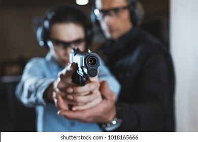 Instructor helping customer in shooting gallery with gun on foreground