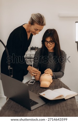 Instructor helping student practice applying individual eyelash extensions on a mannequin head during a beauty school training course