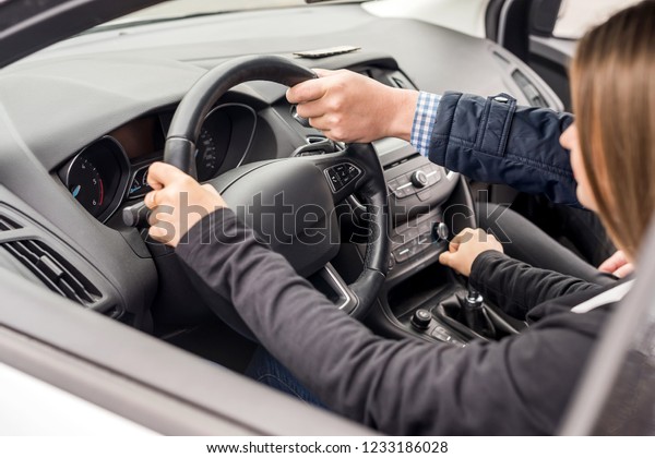 Instructor helping young\
woman drive a car