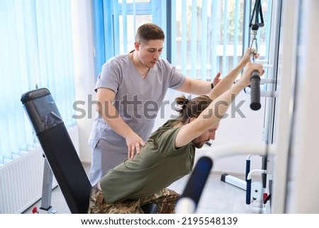 Instructor helps patient to exercise on simulator in rehabilitation sanatorium