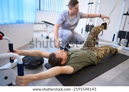 Instructor helps patient to exercise on simulator in military hospital