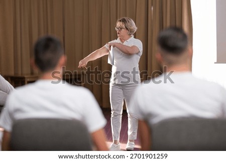 Instructor holding notes and pen while teaching massage therapy class to students, professional training and education in wellness and rehabilitation.