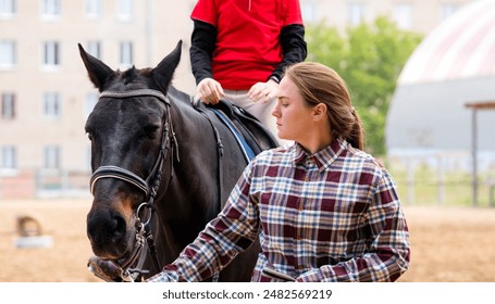 Instructor leads horse while young rider focuses during a riding lesson. Riding school