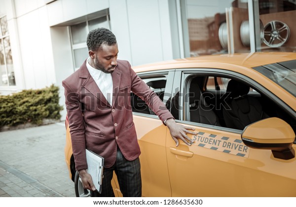 Instructor near car. Experienced\
professional driving instructor standing near nice bright orange\
car