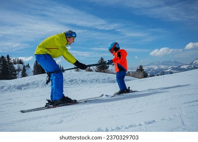 Instructor in skiing school glide backwards teaching little child to ski going downhill holding poles together