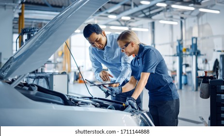 Instructor with a Tablet Computer is Giving a Task for a Future Mechanic. Female Student Inspects the Car Engine. Assistant is Checking the Cause of a Breakdown in the Vehicle in a Car Service. - Powered by Shutterstock