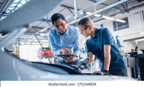 Instructor with a Tablet Computer is Giving a Task for a Future Mechanic. Female Student Inspects the Car Engine. Assistant is Checking the Cause of a Breakdown in the Vehicle in a Car Service. - Powered by Shutterstock