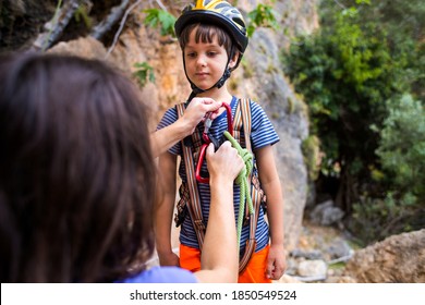 The instructor teaches the child to use climbing equipment, The boy is preparing to climb a rock, A woman shows a child how to use a carabiner for belaying, Mother ties the rope to the safety system. - Powered by Shutterstock