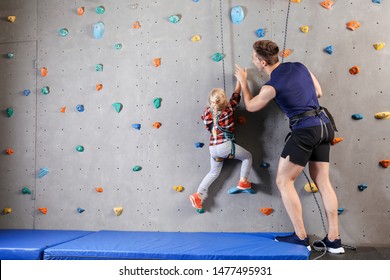 Instructor teaching little girl to climb wall in gym - Powered by Shutterstock