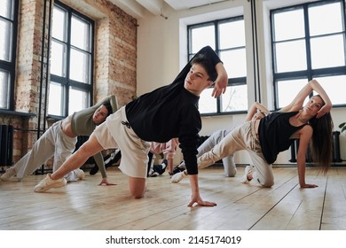 Instructor of vogue dance performance group showing new movements to teenagers in activewear during training in loft studio