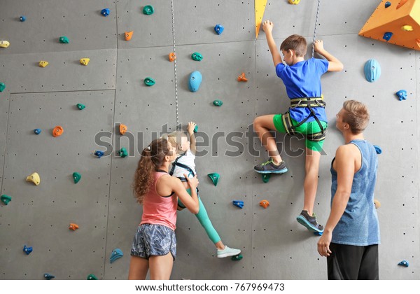Instructors helping\
children climb wall in\
gym