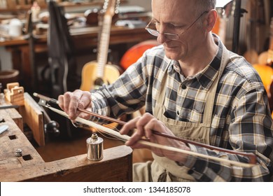 Instrument Maker Inside A Rustic Workshop Is Skillfully Heating The Hair Of A Violin Bow