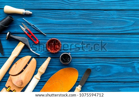 Instruments and materials for make shoes. Shoemaker's work desk. Hummer, awl, knife, sciccors, wooden shoe, insole, paint and leather. Blue wooden background top view copy space
