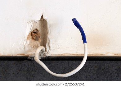 An insulated electrical wire is pulled out of the wall.