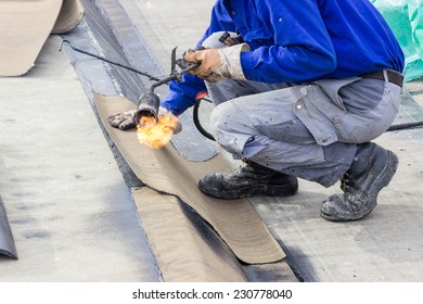 Insulation Worker With Propane Blowtorch At Floor Slab Waterproofing Works. Worker Heating And Melting Bitumen Felt. Water Proofing Of Concrete Structure.