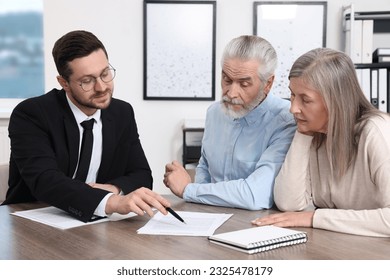 Insurance agent consulting elderly couple about pension plan at wooden table in office - Powered by Shutterstock