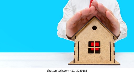 Insurance Agent Covers A Wooden House Model With Both Hands. Property Coverage Concept.