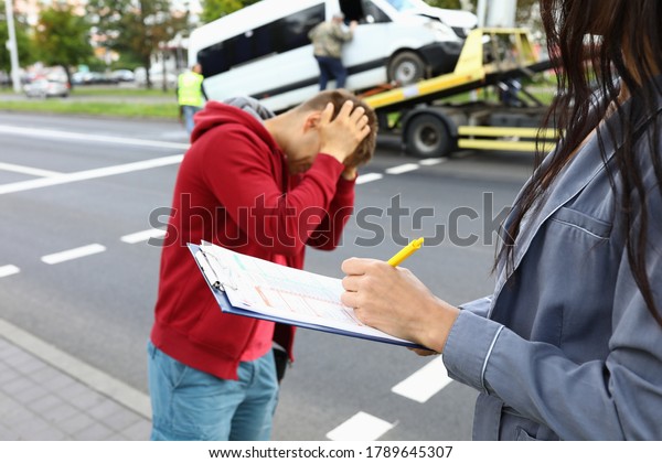 Insurance agent fills out insurance after car\
accident driver is standing next to him and holding his head.\
Services of insurance companies\
concept